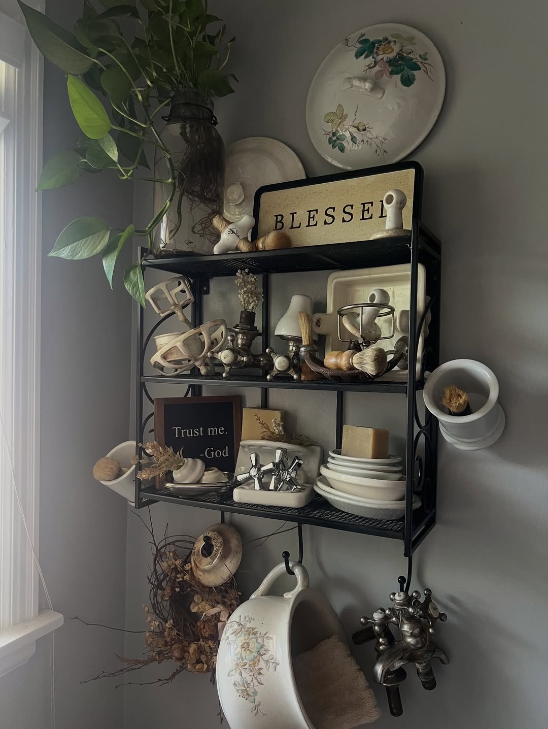 A black metal wall shelf, perfect for vintage farmhouse decor, holds dishes, small signs reading