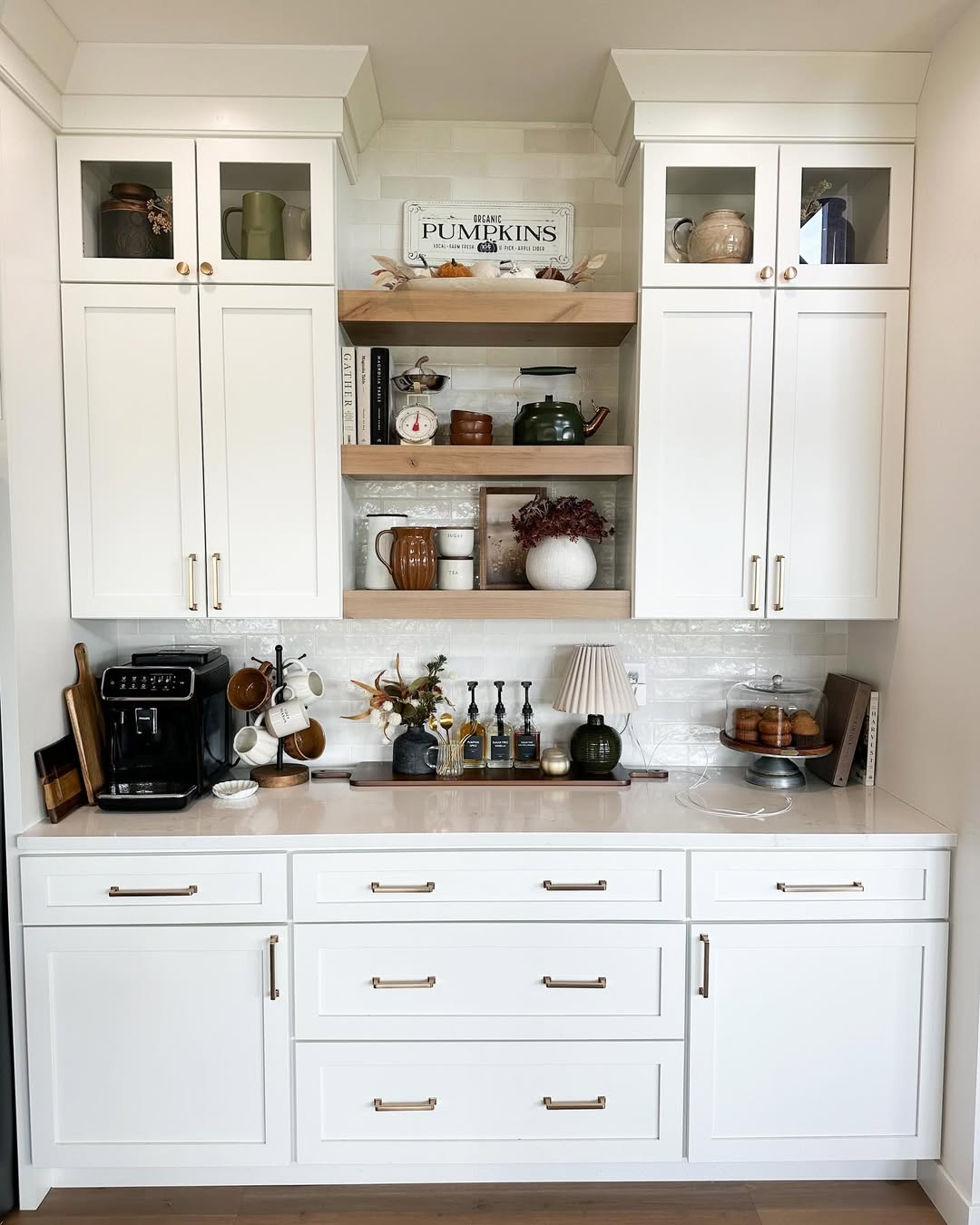 White built-in kitchen hutch with glass and solid cabinets, open shelves holding decor, and a coffee maker—perfect for those seeking kitchen coffee bar ideas to keep countertop chaos at bay. Various kitchen accessories rest neatly on the white countertop.