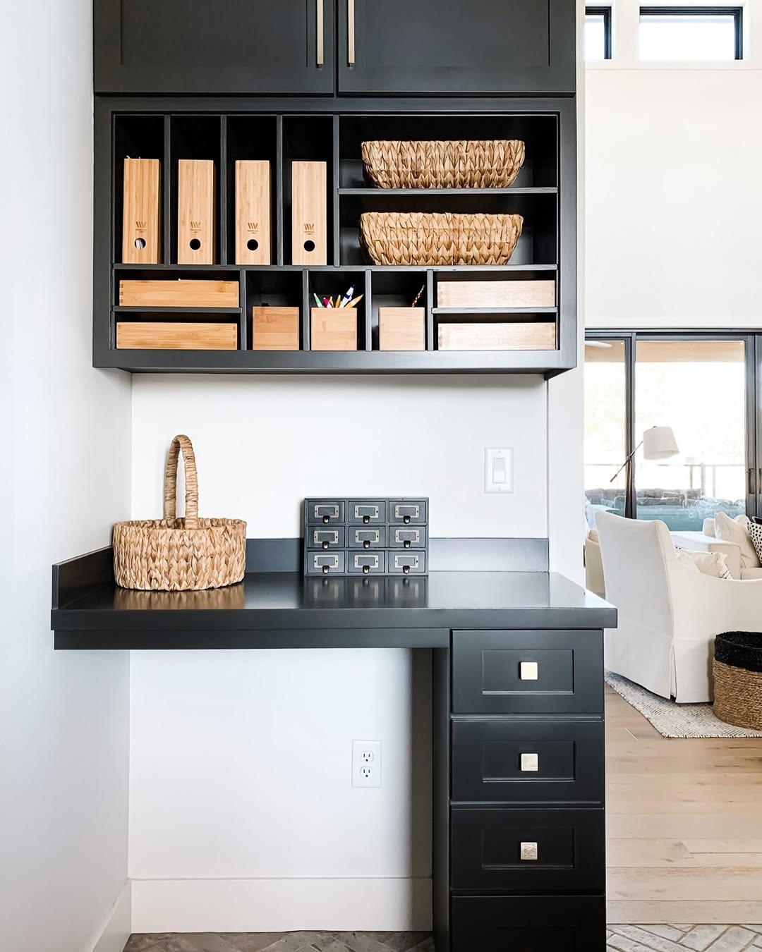 A black desk with matching shelves holds baskets, wooden storage boxes, and a set of drawers—space saving furniture perfect for a bright, modern home office corner.
