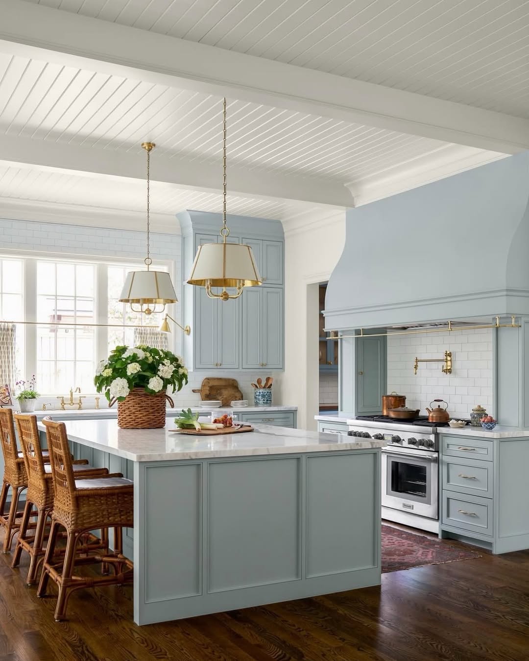 A spacious kitchen with light blue cabinets, a large island with seating, gold accents, white countertops, and wooden flooring. Two pendant lights hang above the island, showcasing modern kitchens and fresh open kitchen ideas.