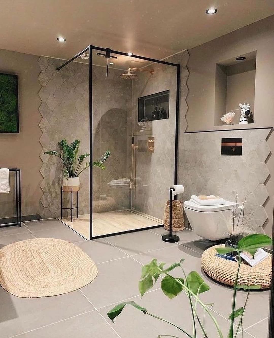 Modern bathroom with a no door shower enclosure, wall-mounted toilet, beige tiles, potted plants, and woven mats—perfect inspiration for small bathrooms.
