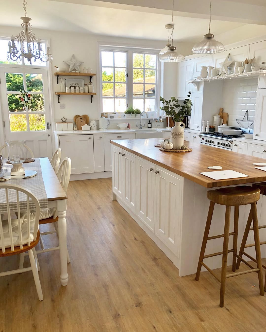 Bright kitchen with white cabinets, a wooden island countertop, dining table with chairs, large windows, and pendant lights—perfect for those seeking modern open kitchen ideas.
