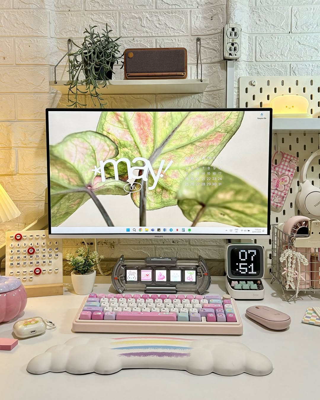 A pastel-themed computer desk setup with a large monitor displaying a May calendar, pastel keyboard, mouse, digital clock, and decorative items—perfect for those seeking stylish Desk Organization and creative Desk Ideas.