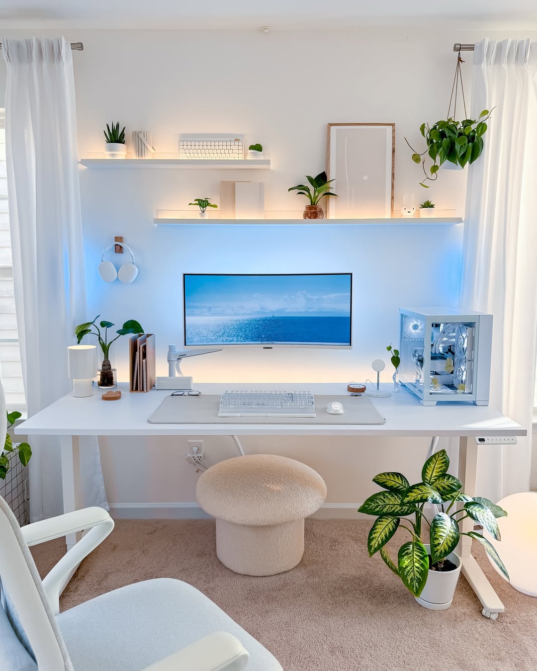 Minimalist home office featuring smart desk organization with a white desk setup, large monitor, PC, plants, and floating shelves for decor against a white wall and curtains.