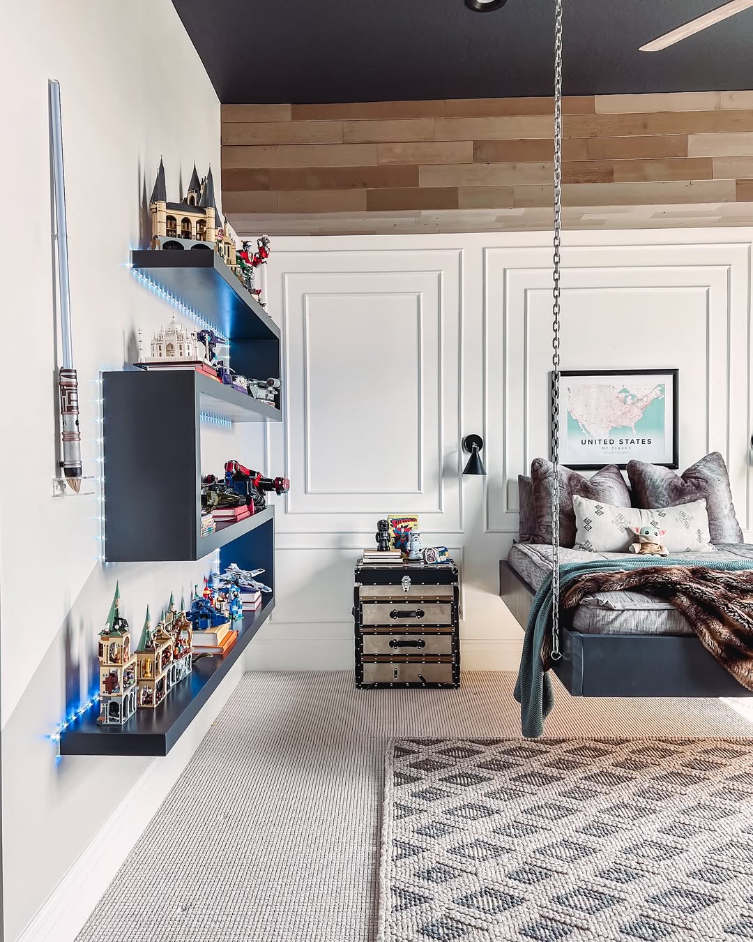 A modern boys bedroom idea featuring floating shelves for LEGO storage, a map of the United States, a suspended bed perfect for sleep, and a striped rug on beige carpet.