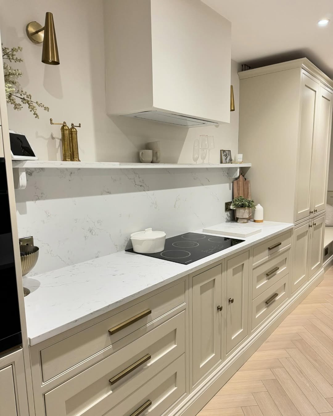 Modern galley kitchen ideas shine with light cream cabinets, brass handles, marble backsplash, induction cooktop, a potted plant, and minimal decorative items on a white shelf—perfect for smart small kitchen design.