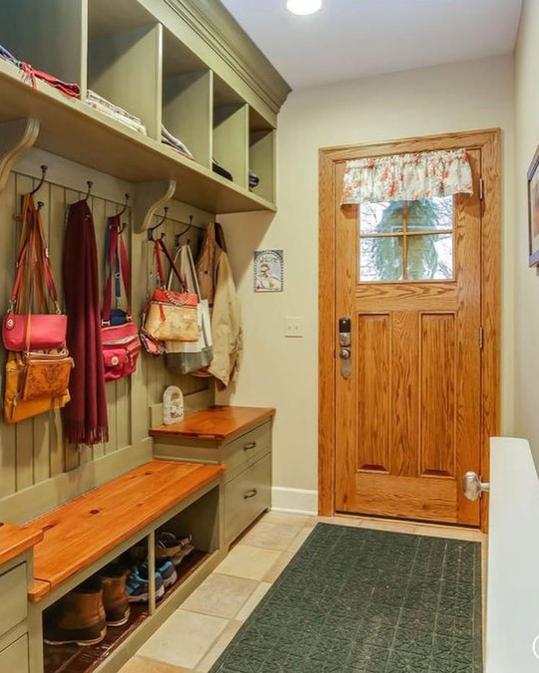 A genius mudroom with wooden benches, cubbies, and hooks neatly storing bags, coats, and scarves—perfect entryway organization. Shoes are stored below, and a wooden door with a window sits to the right for smart mudroom ideas.