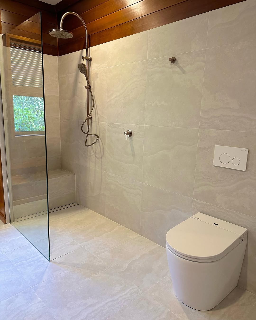 Modern bathroom featuring a no door walk-in shower with a glass divider, built-in bench, white toilet, and light-colored tiled walls and floor—perfect for small bathroom ideas.
