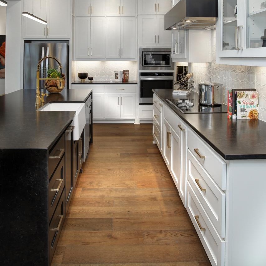 Modern kitchen with white cabinets, dark island, black countertop kitchen, stainless steel appliances, farmhouse sink, and wooden floor. Countertops display decor and kitchen essentials.