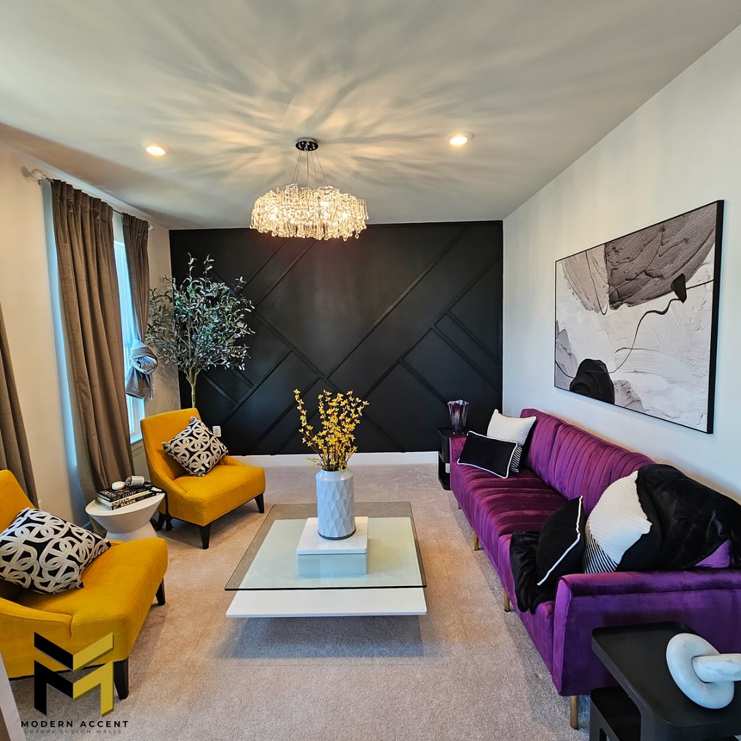 Modern black living room featuring a purple sofa, two yellow chairs, abstract art, a crystal chandelier, and a white coffee table topped with a vase of yellow flowers.
