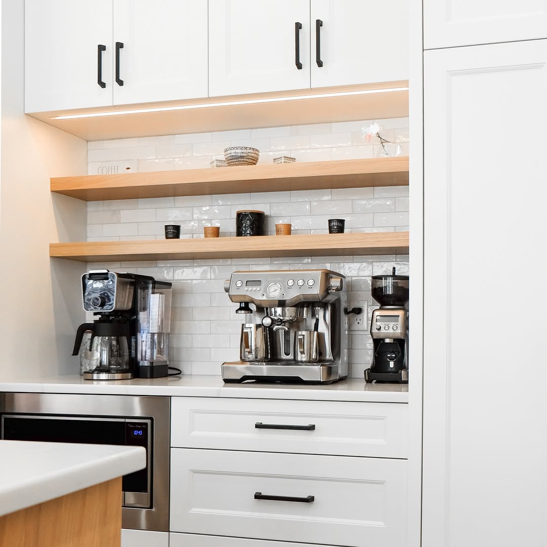Modern kitchen coffee bar with a drip coffee maker, espresso machine, and grinder on a white countertop beneath wooden shelves and cabinets—perfect inspiration for your own kitchen coffee bar ideas without any countertop chaos.