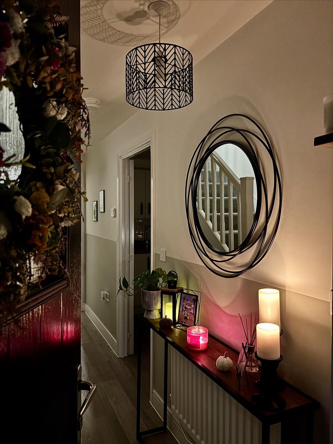 A hallway with a round decorative mirror, a console table holding candles and framed photos, and a modern ceiling light—perfect inspiration for stylish hallway decor. Stairs are visible in the background.