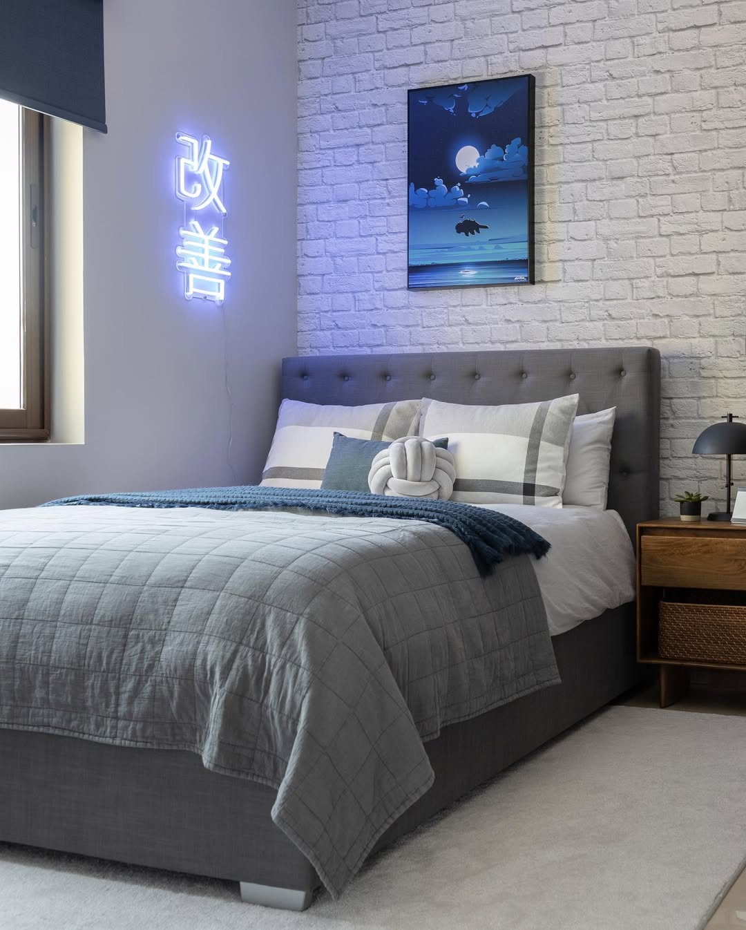 Modern bedroom with a grey bed, white brick accent wall, neon sign with Japanese text, folded towel swan, nightstand, lamp, and framed moonlit ocean artwork—perfect for inspiring boys bedroom ideas and creating a peaceful sleep space.