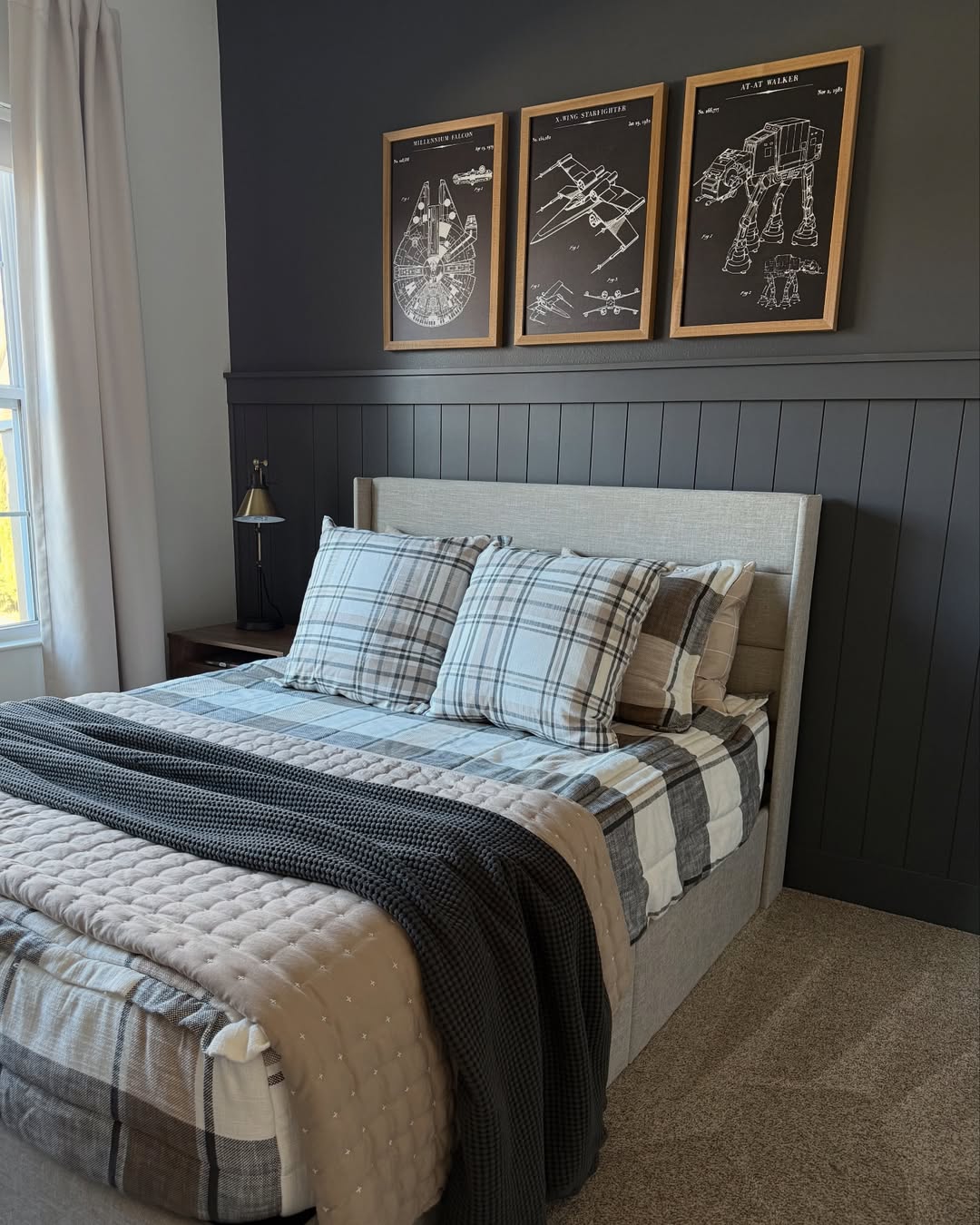 A neatly made bed with plaid bedding sits against a dark accent wall, featuring three framed technical Star Wars posters above the headboard—perfect for sleep and inspiring Boys bedroom ideas.