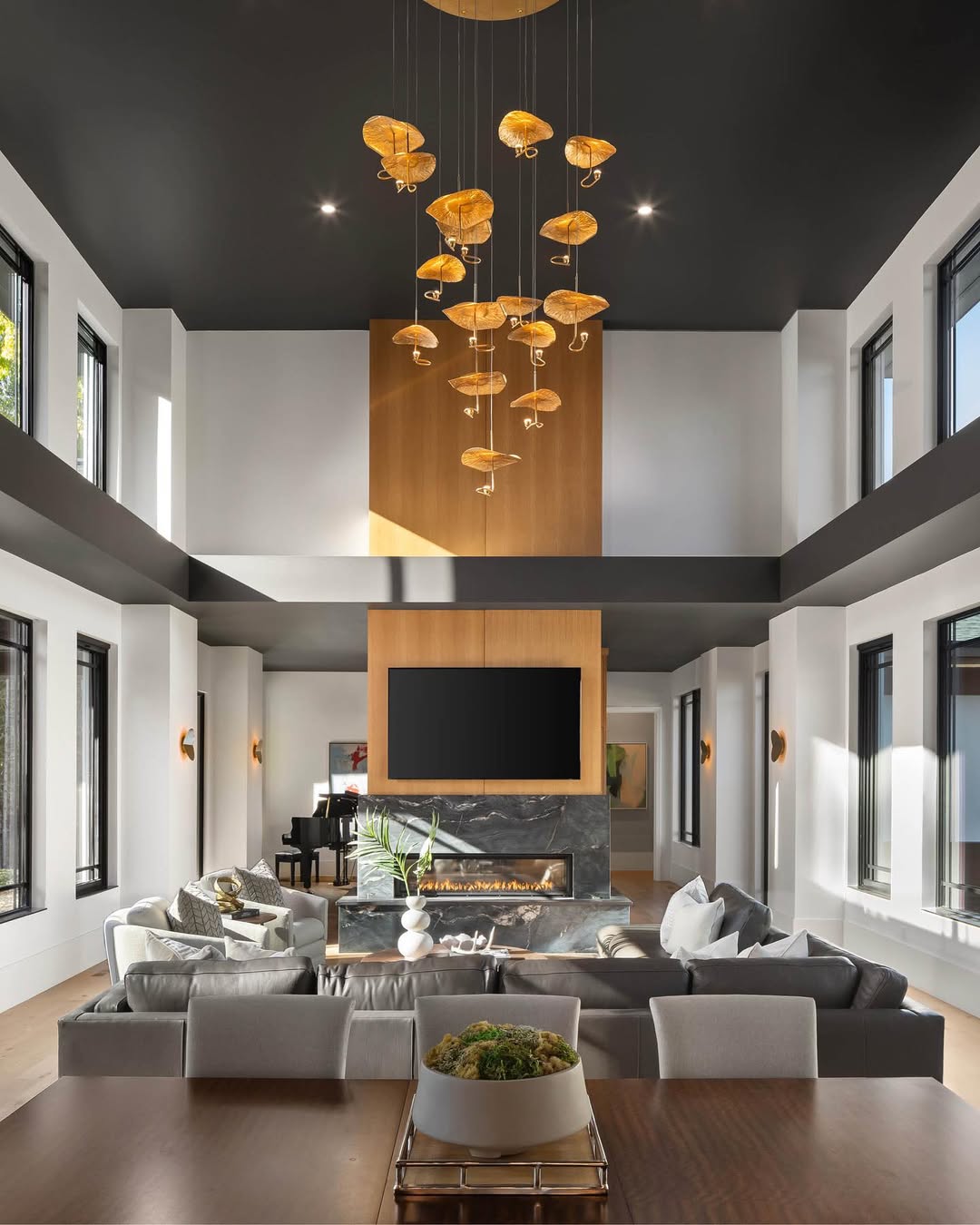 Modern high ceiling living room with clustered gold pendant lights, black-framed windows, a fireplace, and a large wall-mounted TV above a marble surround—perfect inspiration to make your home feel bigger.