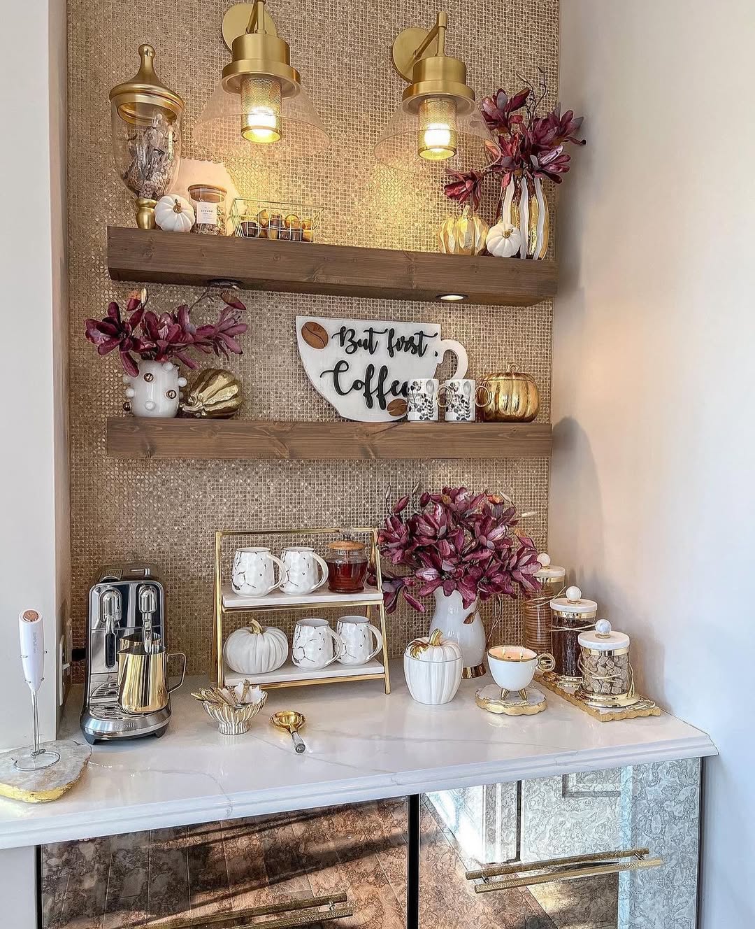 A coffee station with a coffee maker, cups, gold and white decor, artificial purple flowers, and a