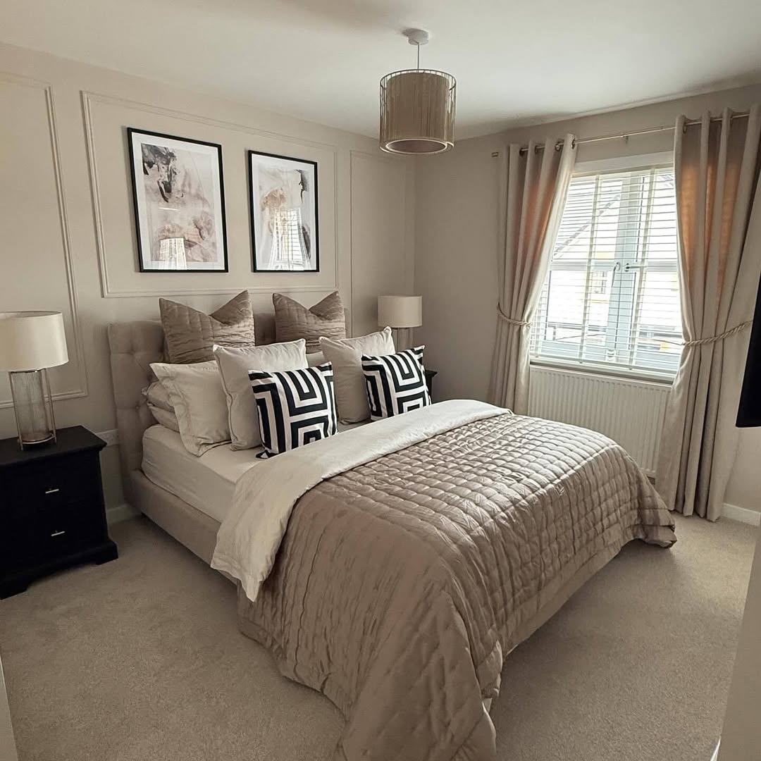 A modern bedroom with a double bed, neutral bedding, geometric pillows, two black nightstands with lamps, framed art above the bed, beige curtains, and a window with blinds—perfect inspiration for guest bedroom ideas.