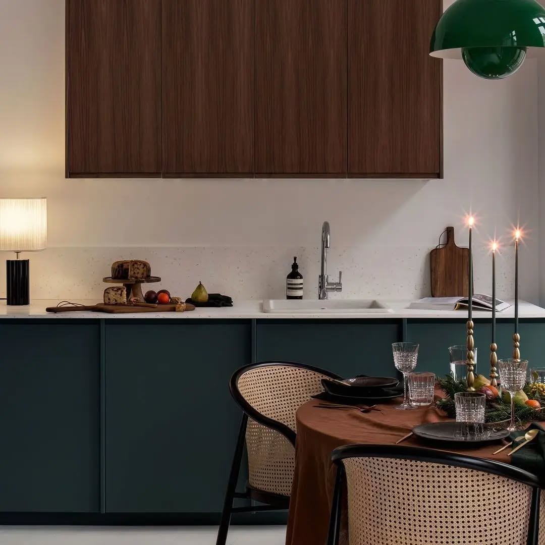 A modern kitchen and dining area with dark cabinets, wood accents, a set dining table with candles, a lamp, and various food items on the counter showcases clever space saving furniture ideas for contemporary living.