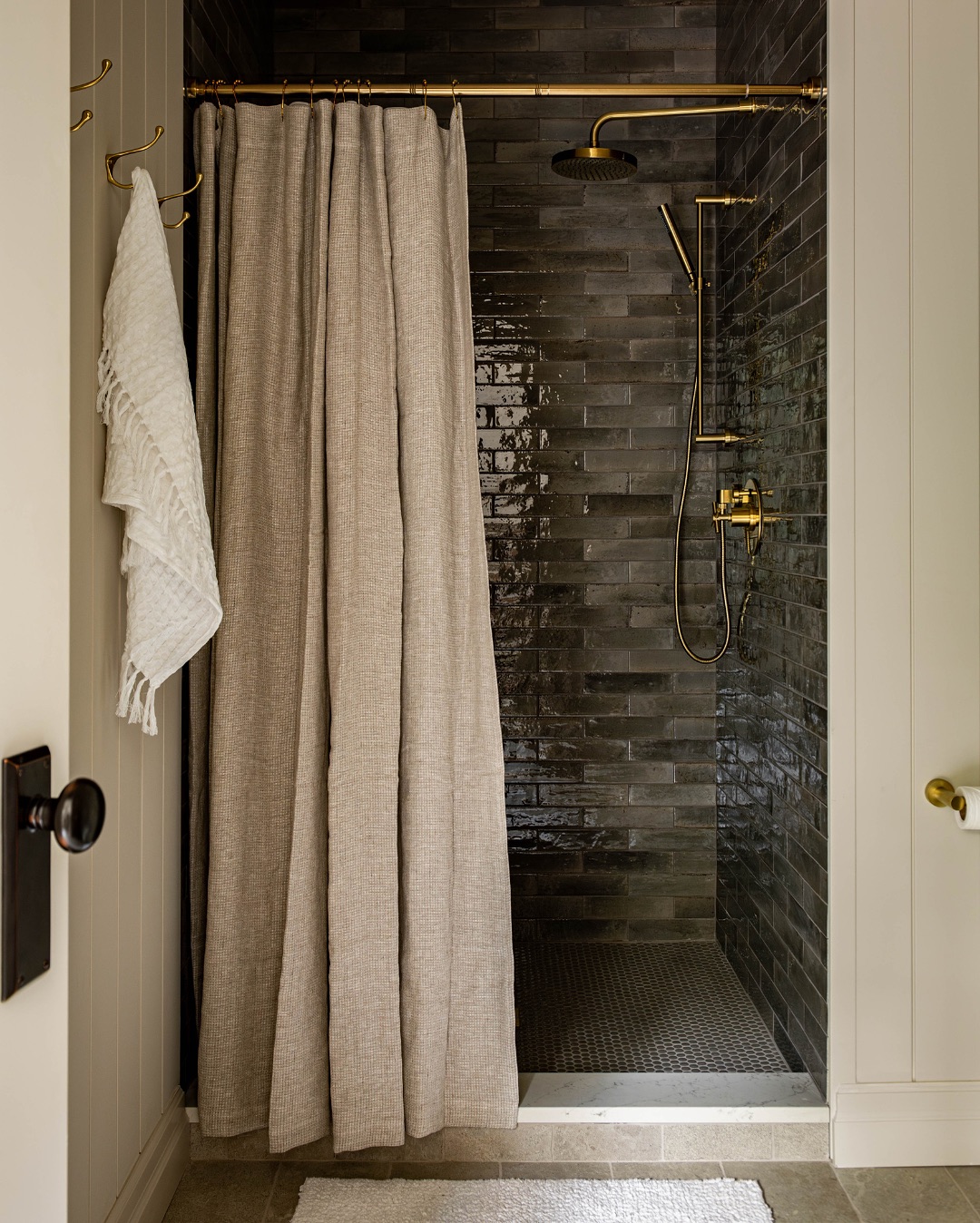 A no door shower with dark tile walls, brass fixtures, and a beige fabric curtain creates a stylish option for small bathrooms. A white towel hangs on a hook outside the shower.