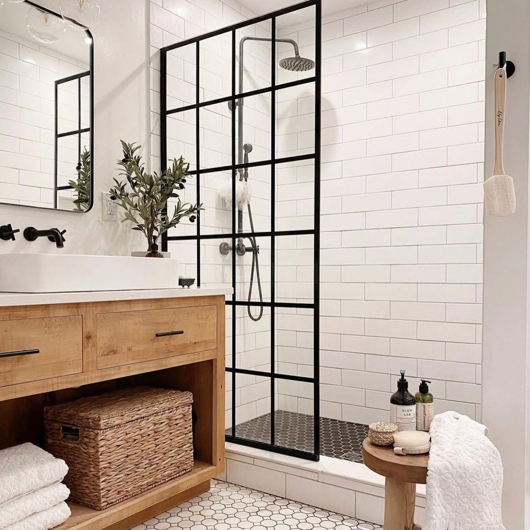 Modern small bathroom with a no door shower featuring a black grid glass frame, wooden vanity with vessel sink, and neatly arranged toiletries on a small round stool for inspiring walk-in shower ideas.