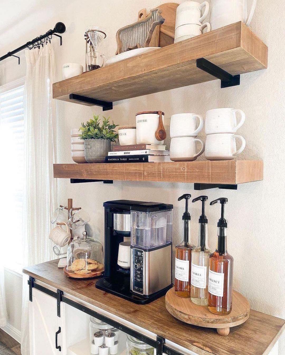 A coffee bar with a coffee maker, syrup bottles, mugs, plates, bowls, potted plant, and kitchen decor arranged on wooden shelves and a countertop—perfect inspiration for your own kitchen coffee bar ideas.