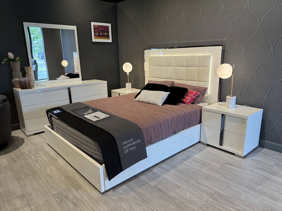 Modern Italian bedroom with a white bed frame, brown bedding, two white nightstands with lamps, and a matching white dresser; abstract wallpaper and wall art complete the stylish look.