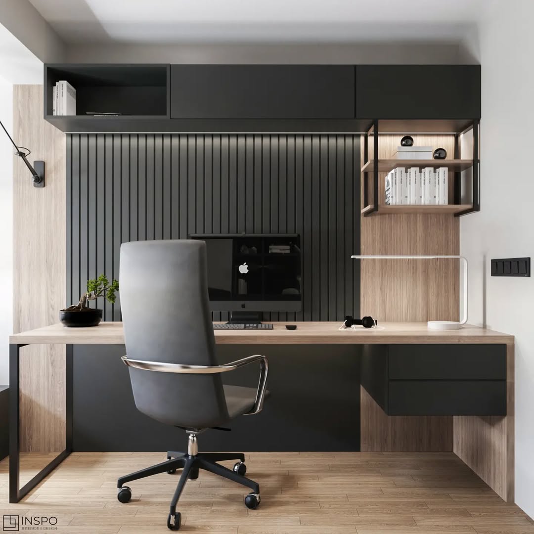 Modern small home office with a black and wood desk, ergonomic chair, wall-mounted shelves, a desktop computer, books, and a desk lamp in a minimalist design.