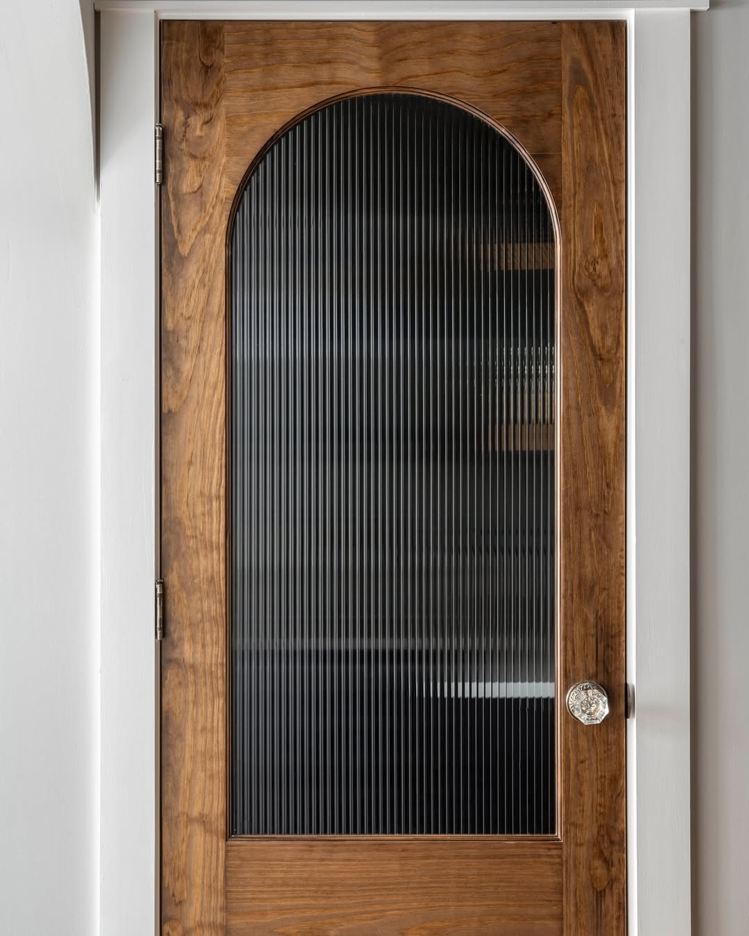 A wooden pantry door with an arched, ribbed glass panel and a round metallic knob, set within a white door frame—perfect for adding charm to your kitchen decor.