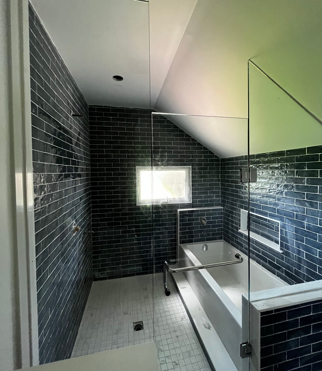 Modern bathroom with dark subway tile walls, a white bathtub with a metal grab bar, no door shower, glass enclosure, and a small window providing natural light—perfect inspiration for small bathrooms.