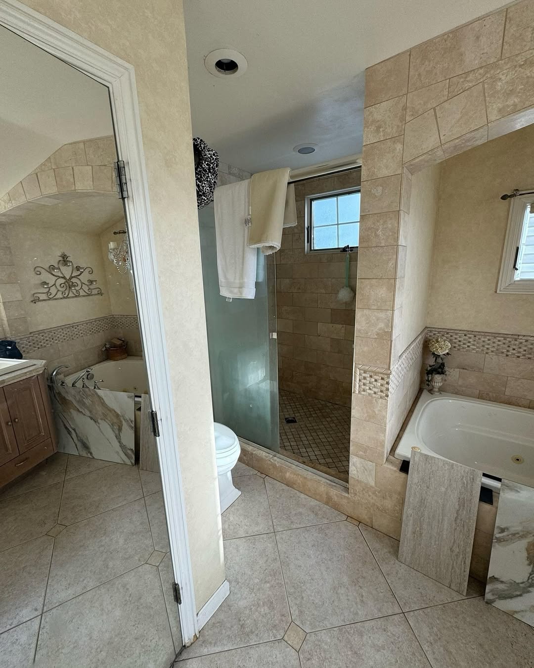 A bathroom with tiled walls and floor, a bathtub, toilet, vanity with sink, towels hanging over the shower door, and a glass no door walk-in shower—perfect for small bathrooms and modern bathroom ideas.