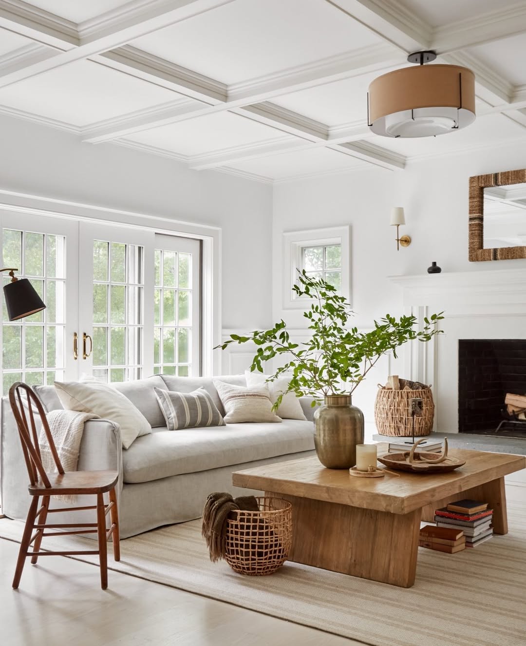 Bright living room with a white sofa, wooden coffee table, decorative vases, books, baskets, large windows, and neutral decor accents—perfect for island decor inspiration and fresh living room ideas.