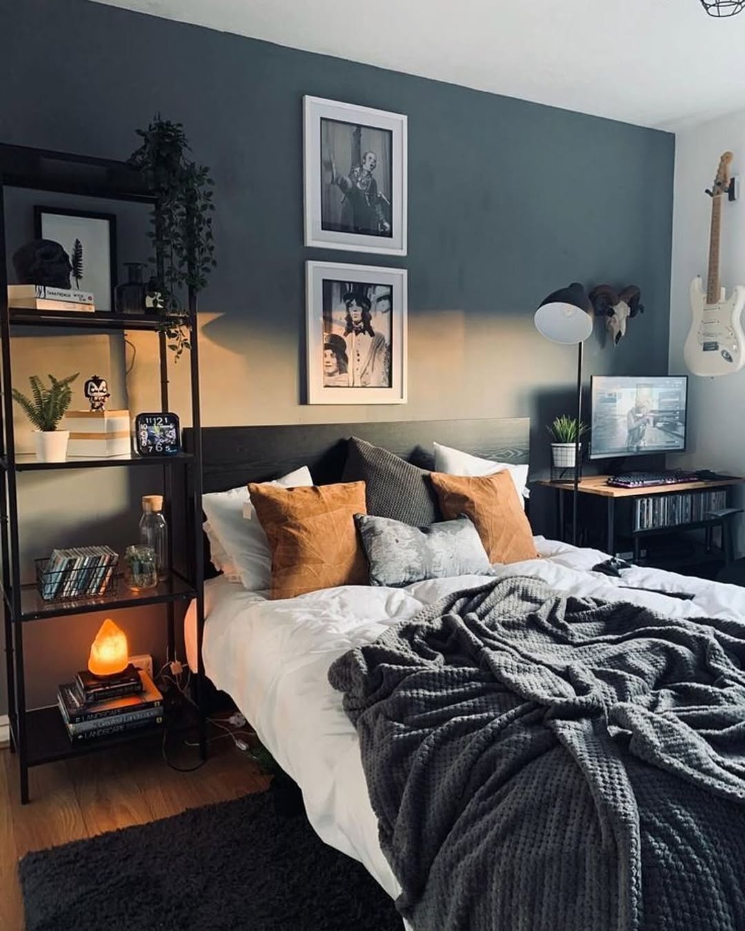 A modern boys bedroom with a gray accent wall, neatly made bed for restful sleep, brown pillows, open shelving for storage solutions, a desk with computer, wall art, and a guitar mounted on the wall.