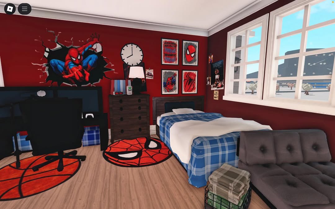 A neatly arranged boys bedroom with red walls decorated with Spider-Man posters, a bed with blue plaid bedding, a desk, clever storage solutions, a gray futon, and Spider-Man-themed rugs.