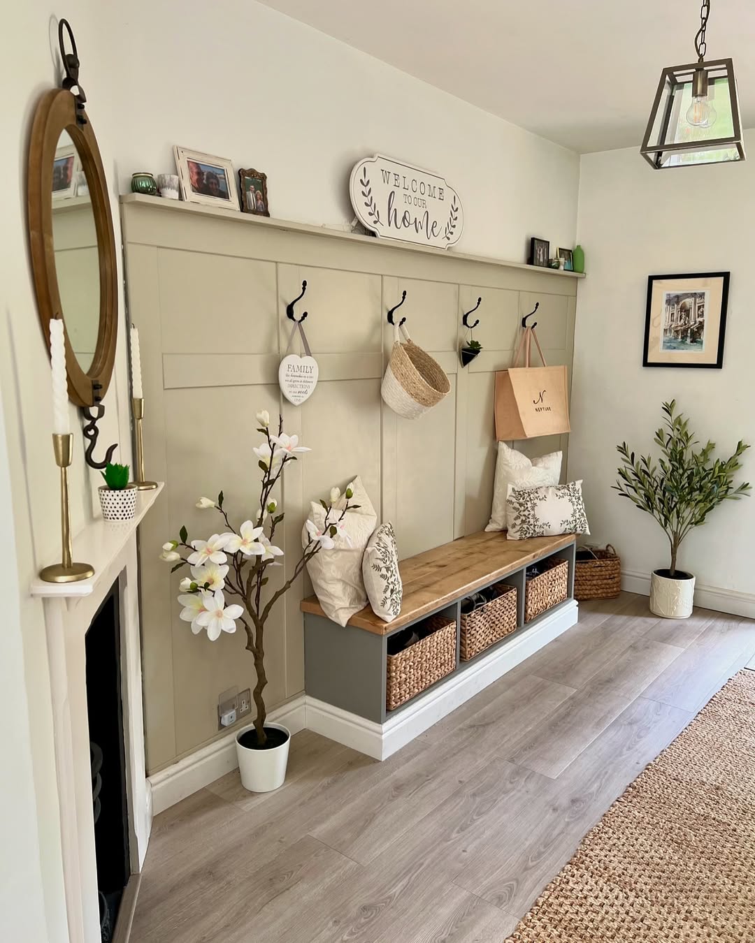A tidy mudroom with a wooden bench, storage baskets, wall hooks holding hats and bags, decorative pillows, framed photos, a mirror, and indoor plants—perfect inspiration for hallway entrance ideas and stylish entryway design.