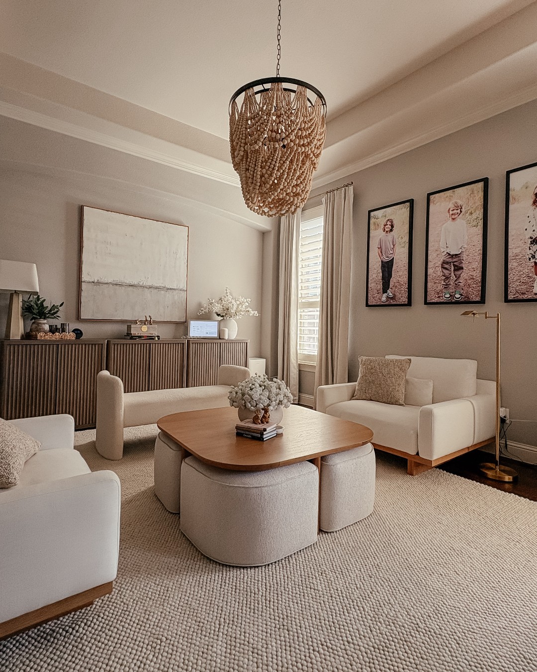 A modern living room with neutral-toned furniture, a wooden coffee table, a beaded chandelier, and framed photos of children on the wall highlights clever space saving furniture ideas for stylish and organized living.