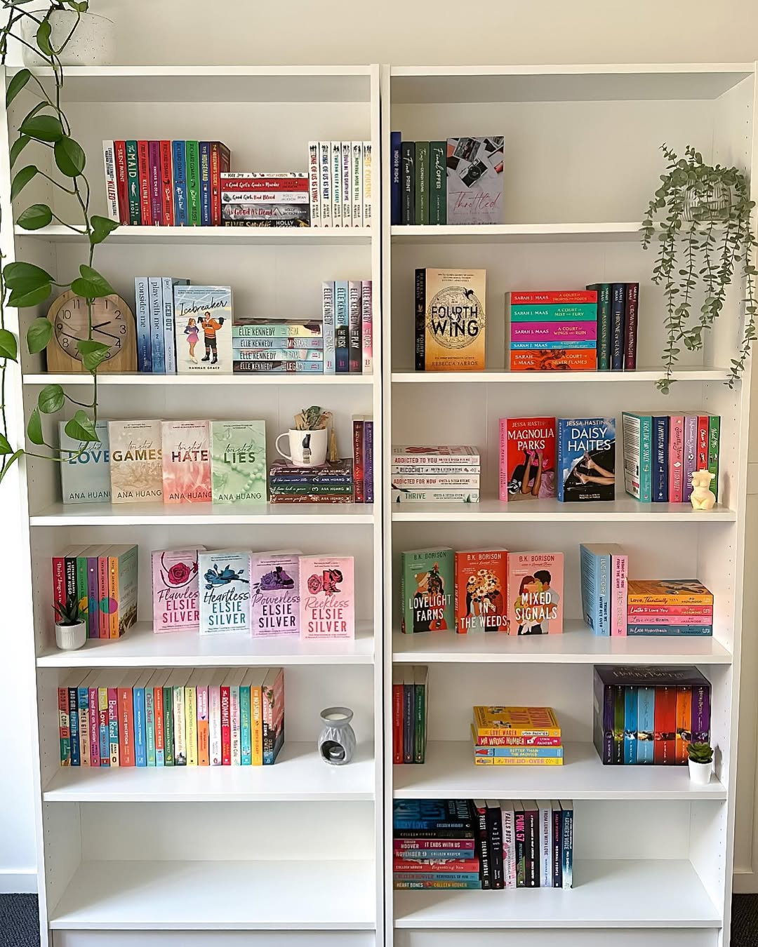 Two white bookshelves filled with neatly arranged colorful books, small plants, and minimal decor showcase clever bookshelf styling ideas against a white wall in a well-lit room.