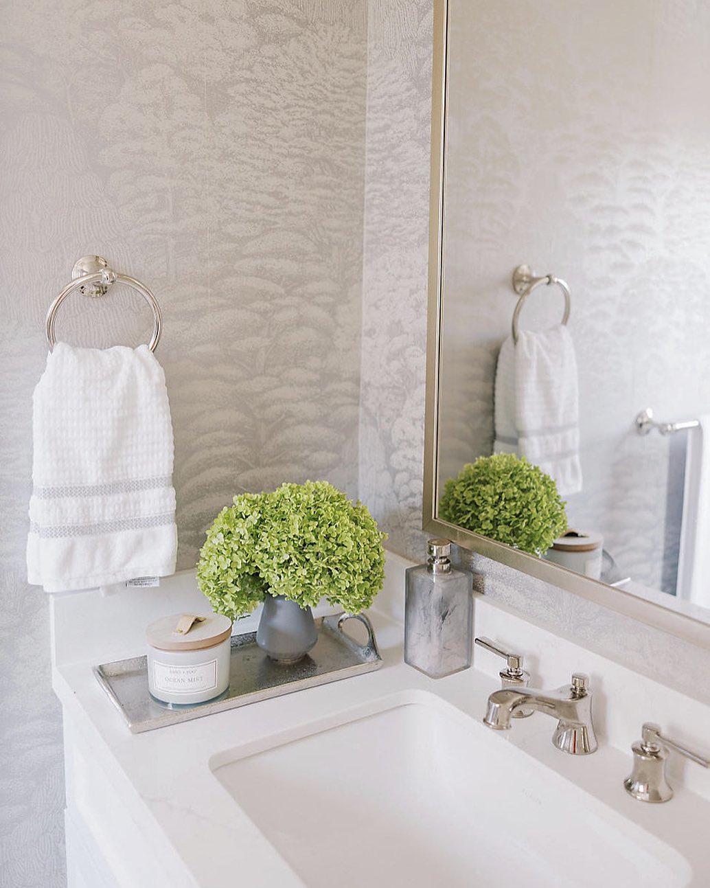 Bathroom vanity with a white towel on a ring, a candle, a small green floral arrangement, a soap dispenser, and a large mirror above the sink—perfect for stylish powder rooms seeking that wow-factor.