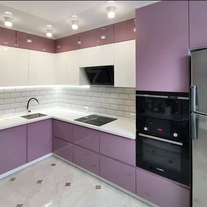 A purple kitchen featuring modern cabinets in a blend of purple and white, black appliances, and a stainless steel fridge. The space is accented with a white subway tile backsplash and boasts a marble floor with an eye-catching geometric design.