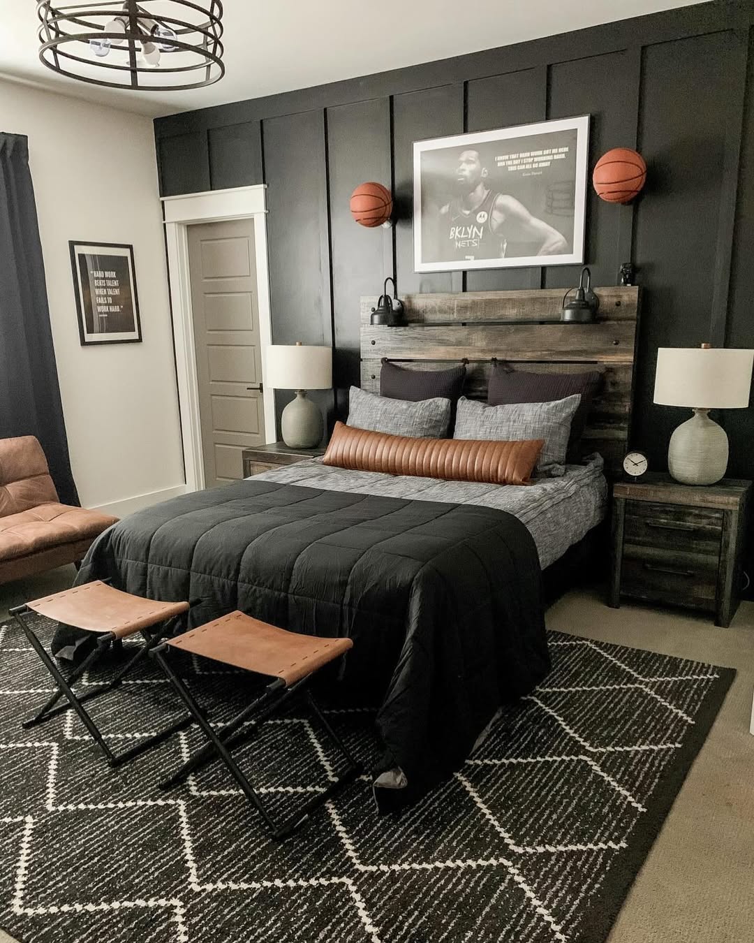 A modern boys bedroom featuring a dark accent wall, basketball decor, smart bedroom design with storage solutions, a bed with gray and brown bedding, two lamps, and two brown stools at the foot of the bed.