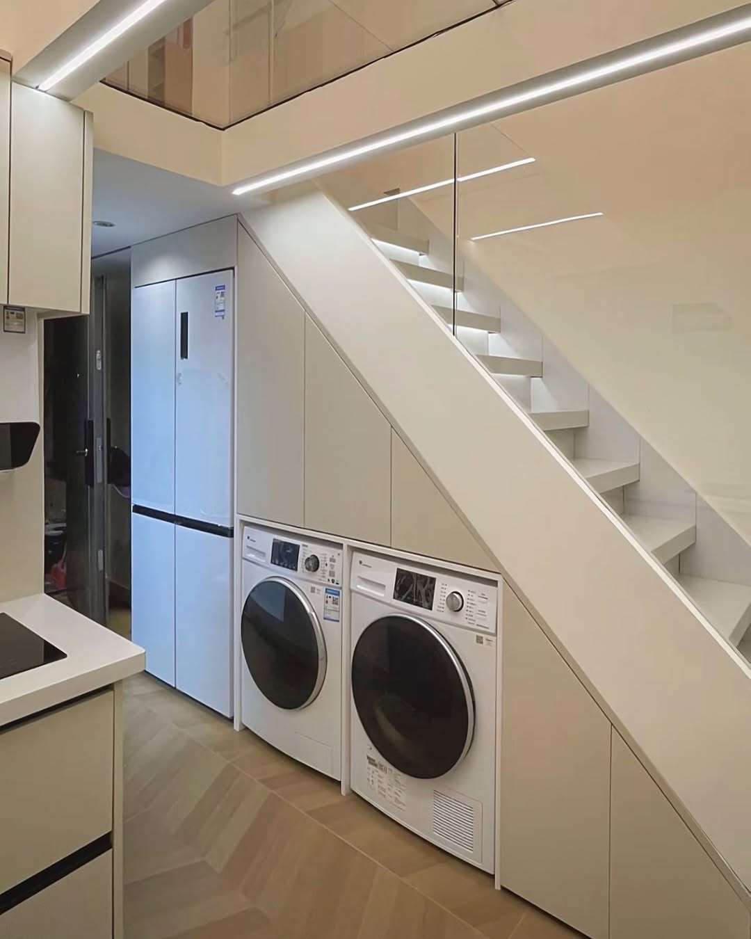 Modern under stair laundry room featuring a washing machine and dryer side by side, white cabinets, and minimalistic design.