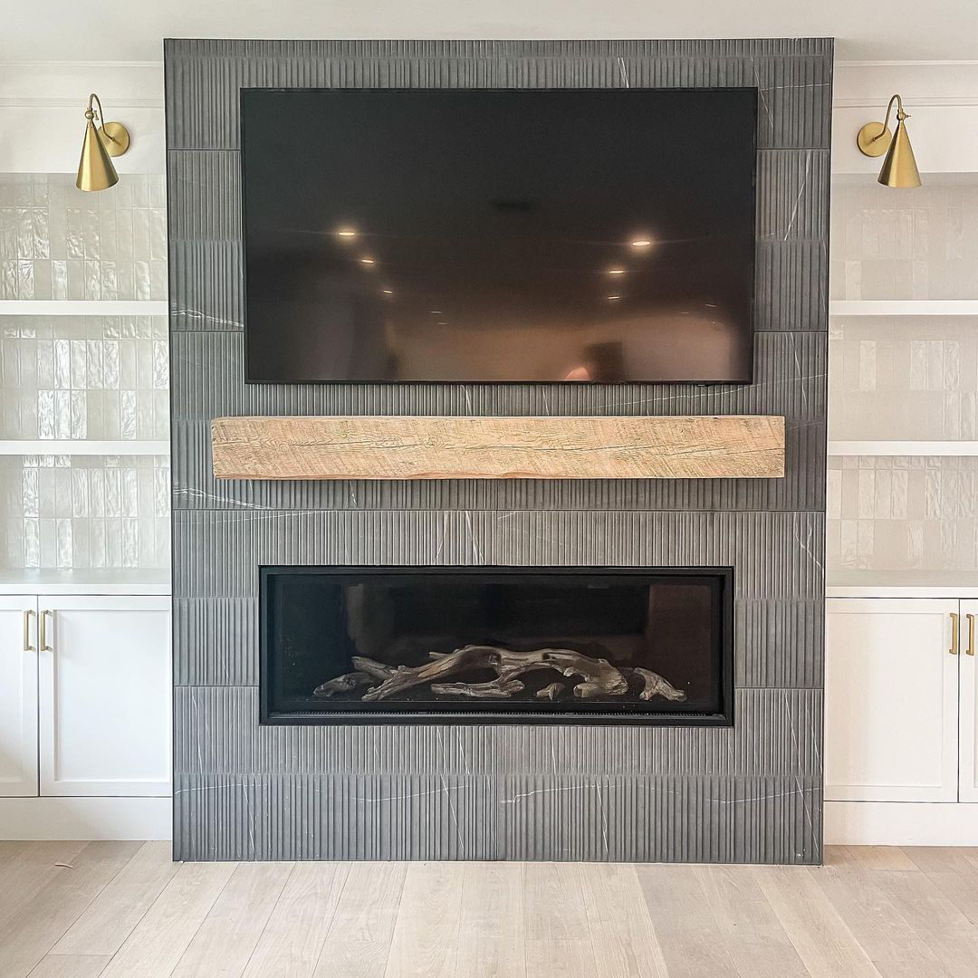 A modern living room features a wall-mounted TV above a wooden mantel and a black linear fireplace showcasing sleek fireplace design, flanked by white built-in shelves and gold wall sconces.