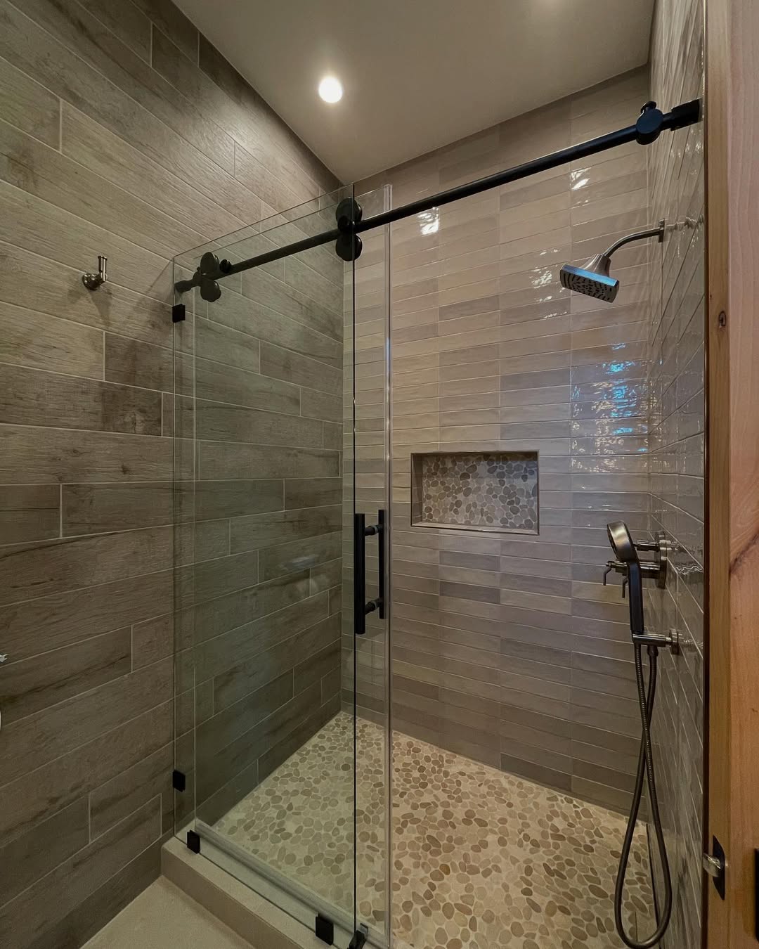 Modern walk-in shower with glass doors, a rainfall showerhead, hand-held sprayer, built-in niche, and stone tile floor—perfect inspiration for small bathrooms seeking stylish walk-in shower ideas.