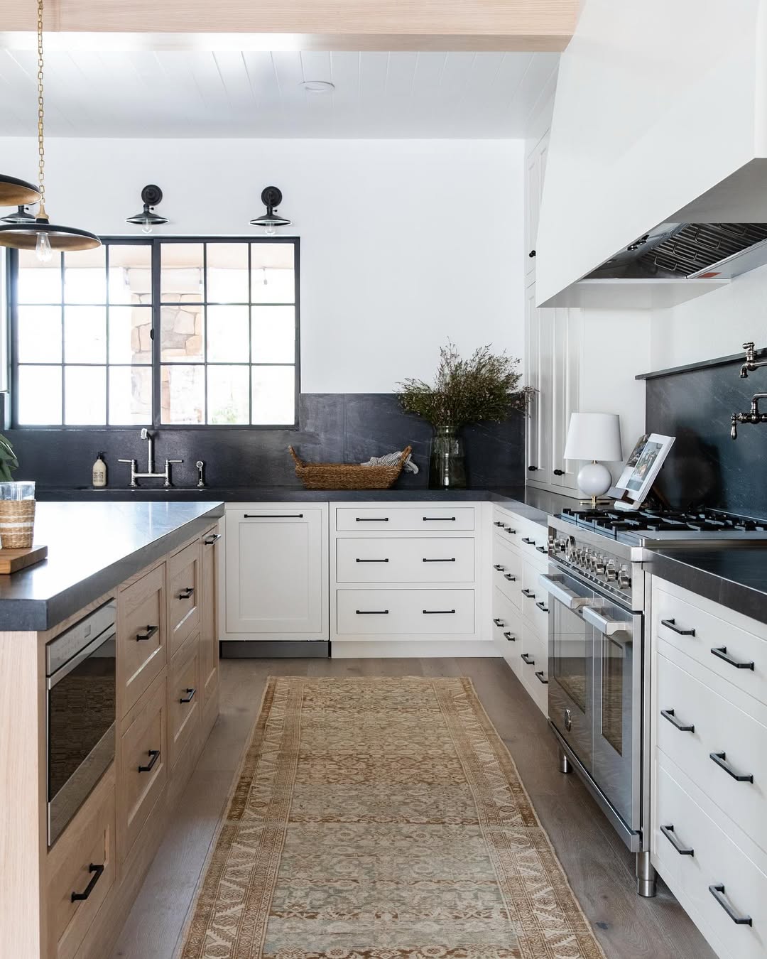 Modern black countertop kitchen with light wood and white cabinets, stainless steel appliances, a cozy rug on the floor, and decorative items displayed on the counter.