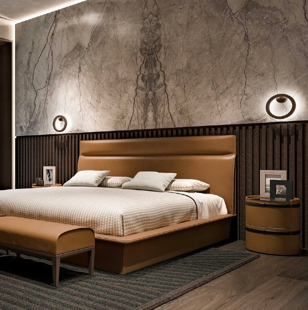 A modern Italian bedroom with a large brown bed, matching bench, round nightstands, marble accent wall, and circular wall lights.