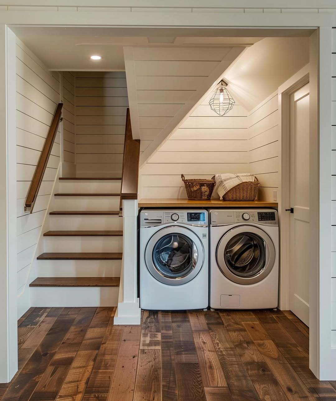 A stylish under stair laundry room features a front-load washer and dryer, with baskets and folded towels neatly arranged on the wooden counter above.