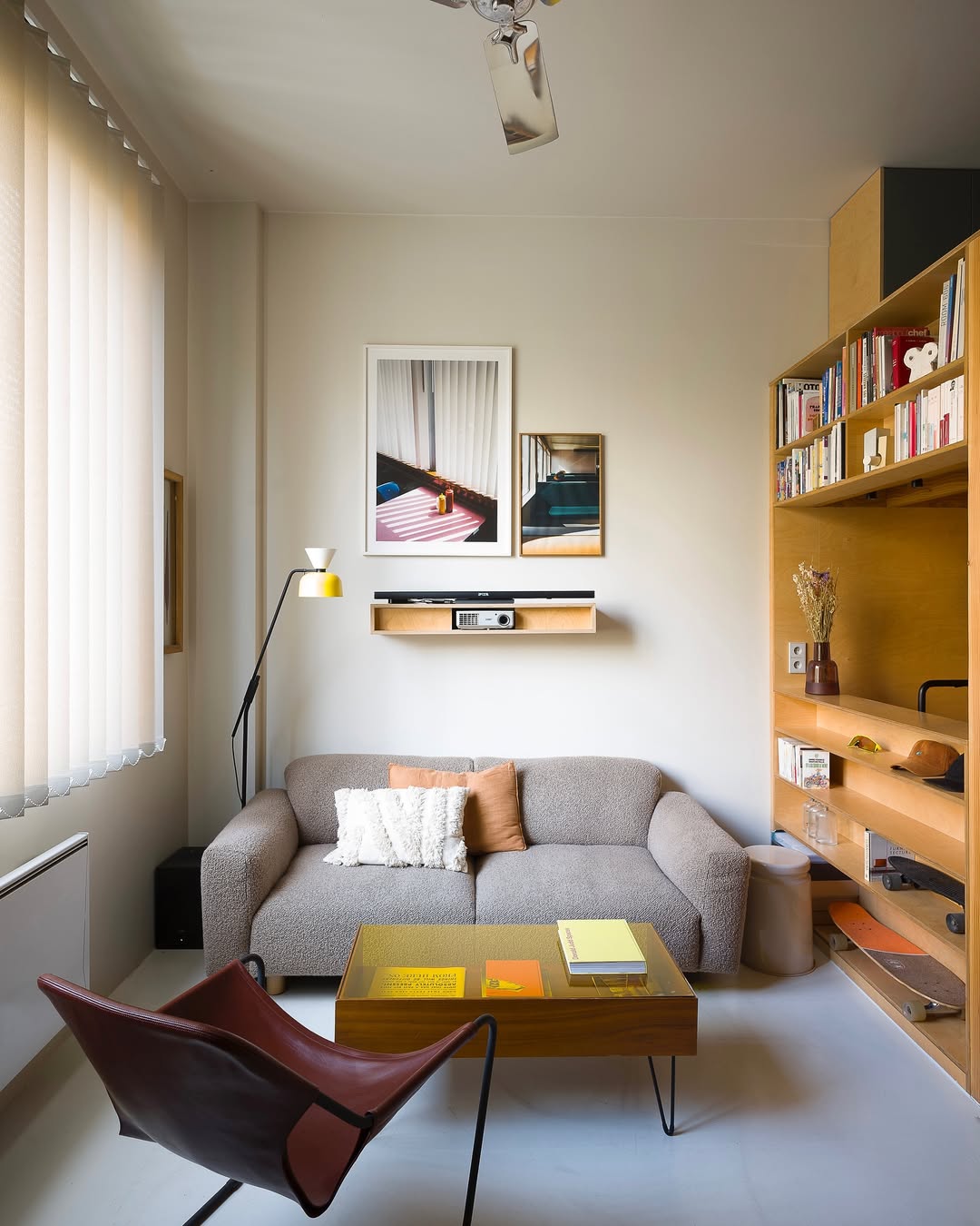 A small living room with a gray sofa, a brown lounge chair, a wooden coffee table with books, wall art, a floor lamp, and a bookshelf filled with books and decor items—perfect inspiration for Small Space Decorating and Tiny Apartment Ideas.