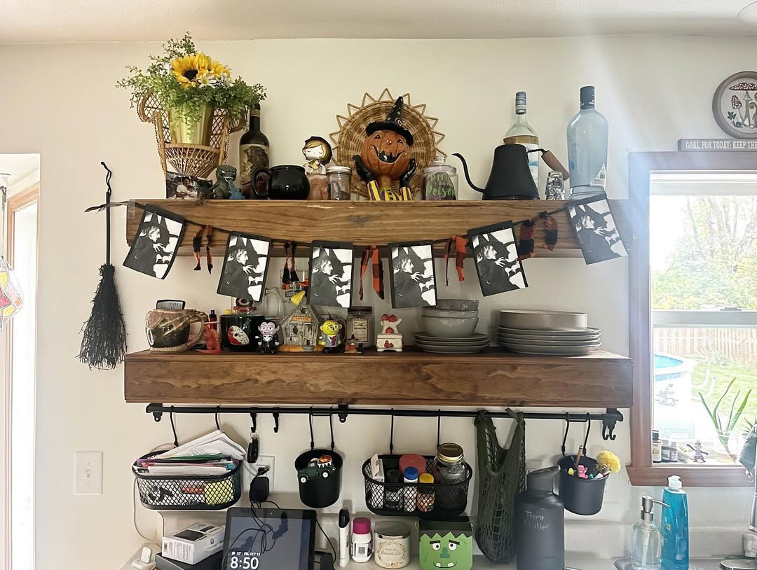 Two wooden kitchen shelves display dishes, mugs, jars, and festive Halloween kitchen decor, plus a small black-and-white photo banner—perfect inspiration for fresh Halloween decor ideas in your kitchen. Baskets and utensils hang below.
